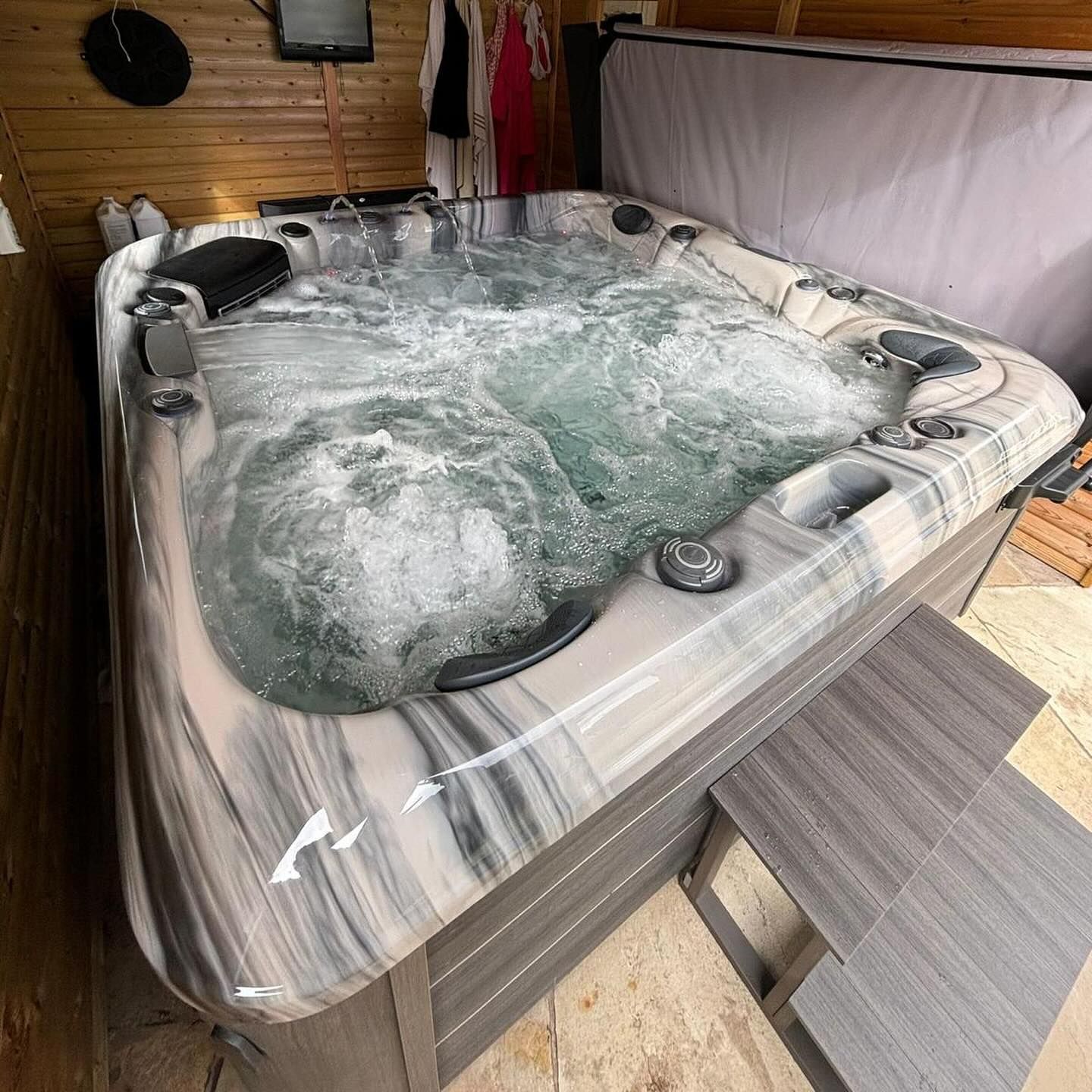 Hot tub with bubbling water, set in a wooden enclosure with gray marbled sides and steps.