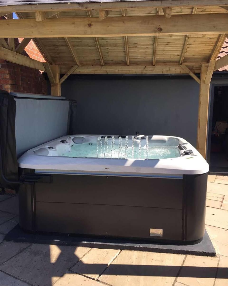 Hot tub under a wooden pergola, partially covered. Spa is filled with water, next to a closed cover.
