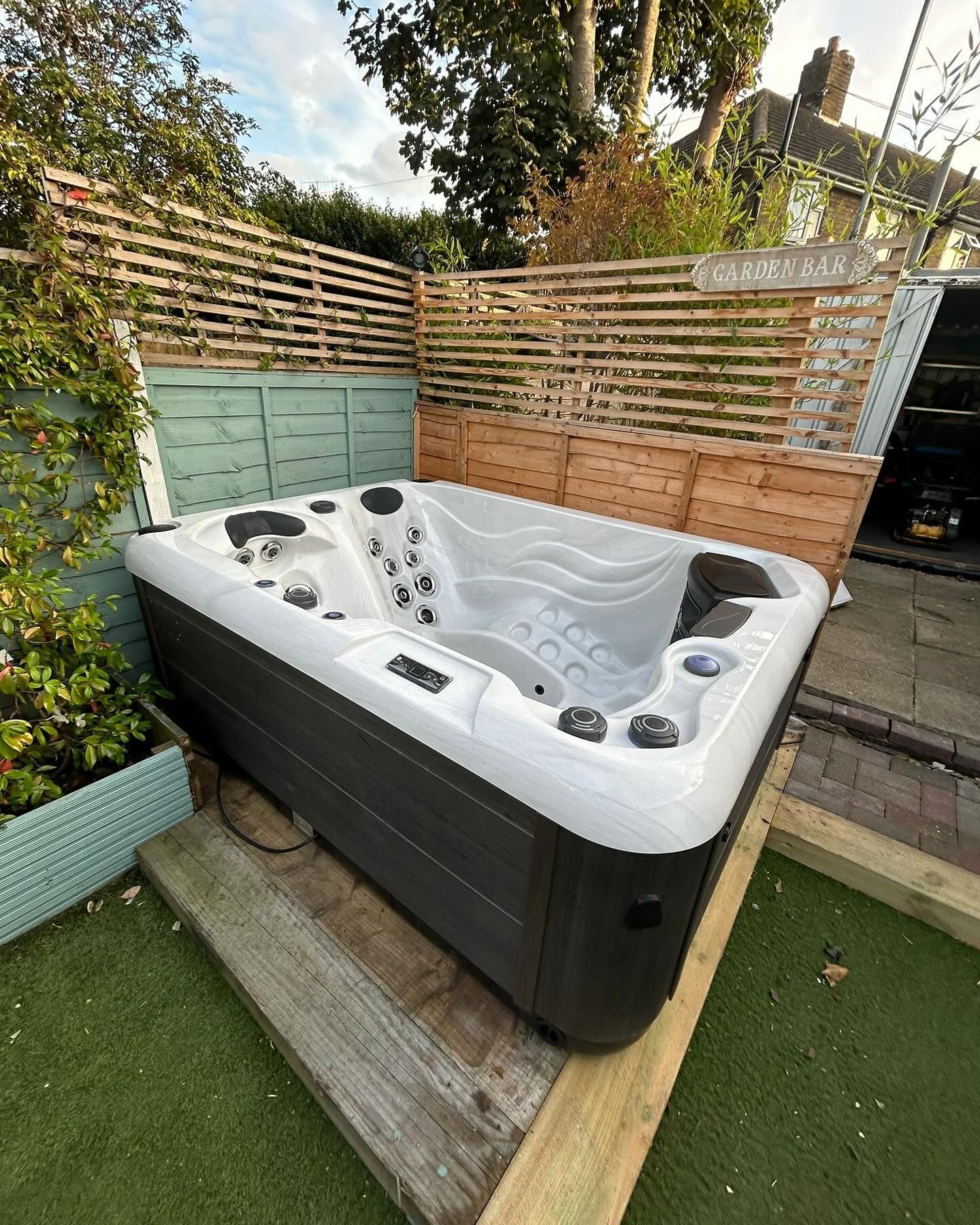 Hot tub in a backyard setting, next to a wooden fence.