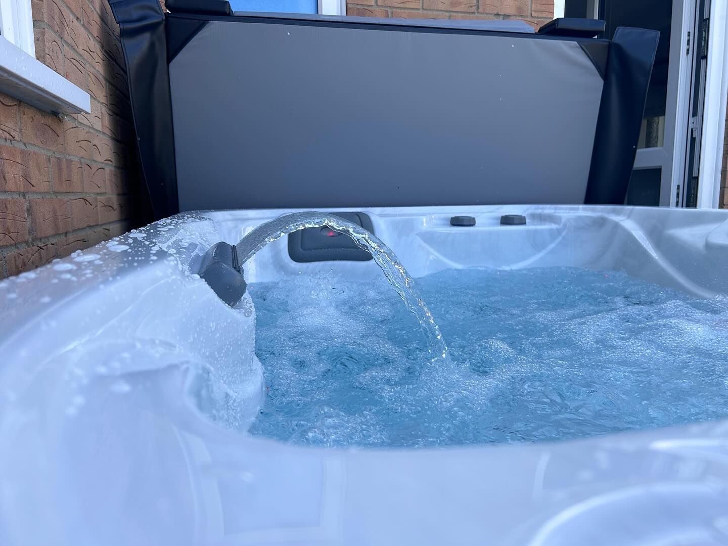 A hot tub with water jets, filled with clear water, and a partially open cover.