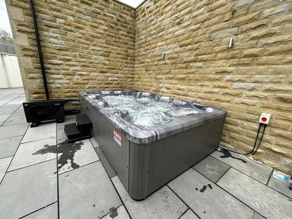 Hot tub on a stone patio next to a brick wall. Water is bubbling. Small steps leading into the tub.