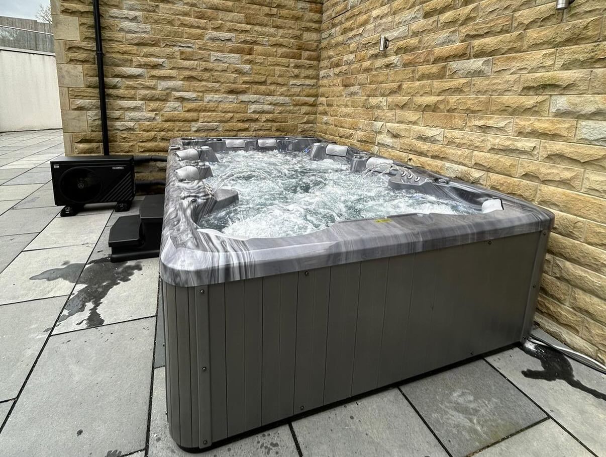 Hot tub with bubbling water on stone patio next to a light-colored brick wall.