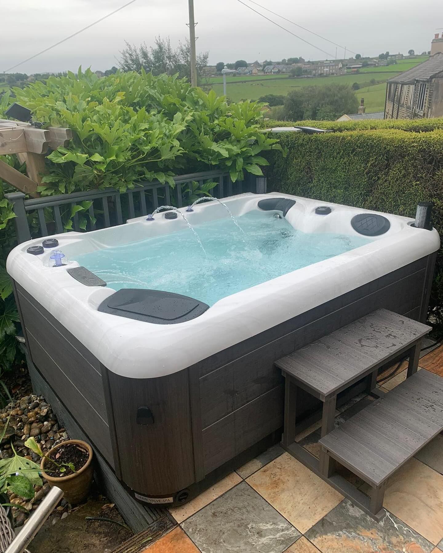 Hot tub with bubbling water on a patio, surrounded by hedges and steps leading up to it.