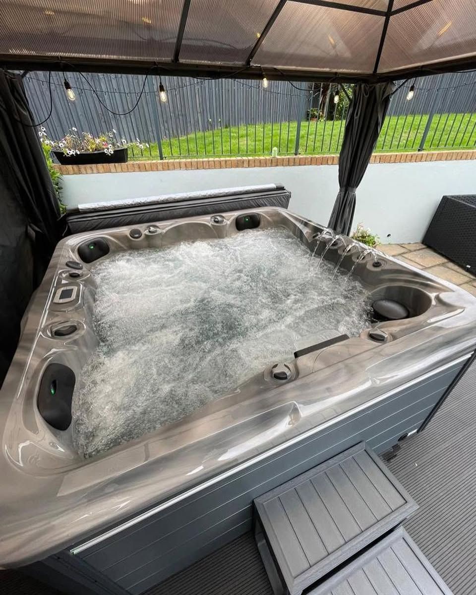 Hot tub with bubbling water under a gazebo with string lights; set on patio with steps.