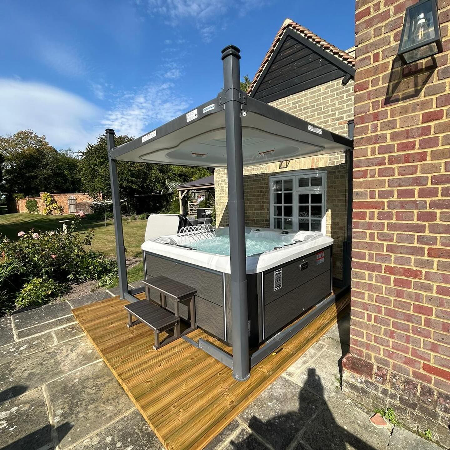 Hot tub under a canopy next to a brick building on a wooden deck.