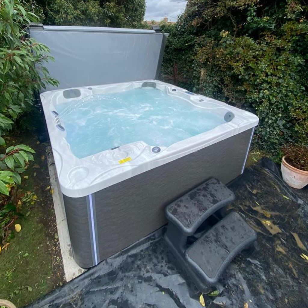 Hot tub with cover open, surrounded by greenery. Steps are in front.