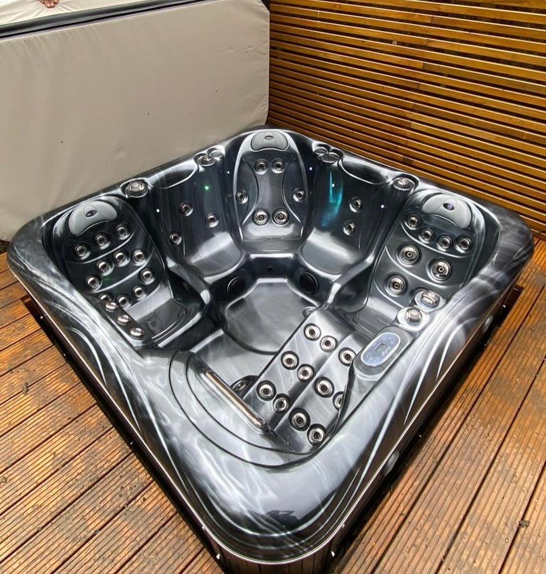 Black hot tub on wooden deck, cover partially open, surrounded by wood paneling.