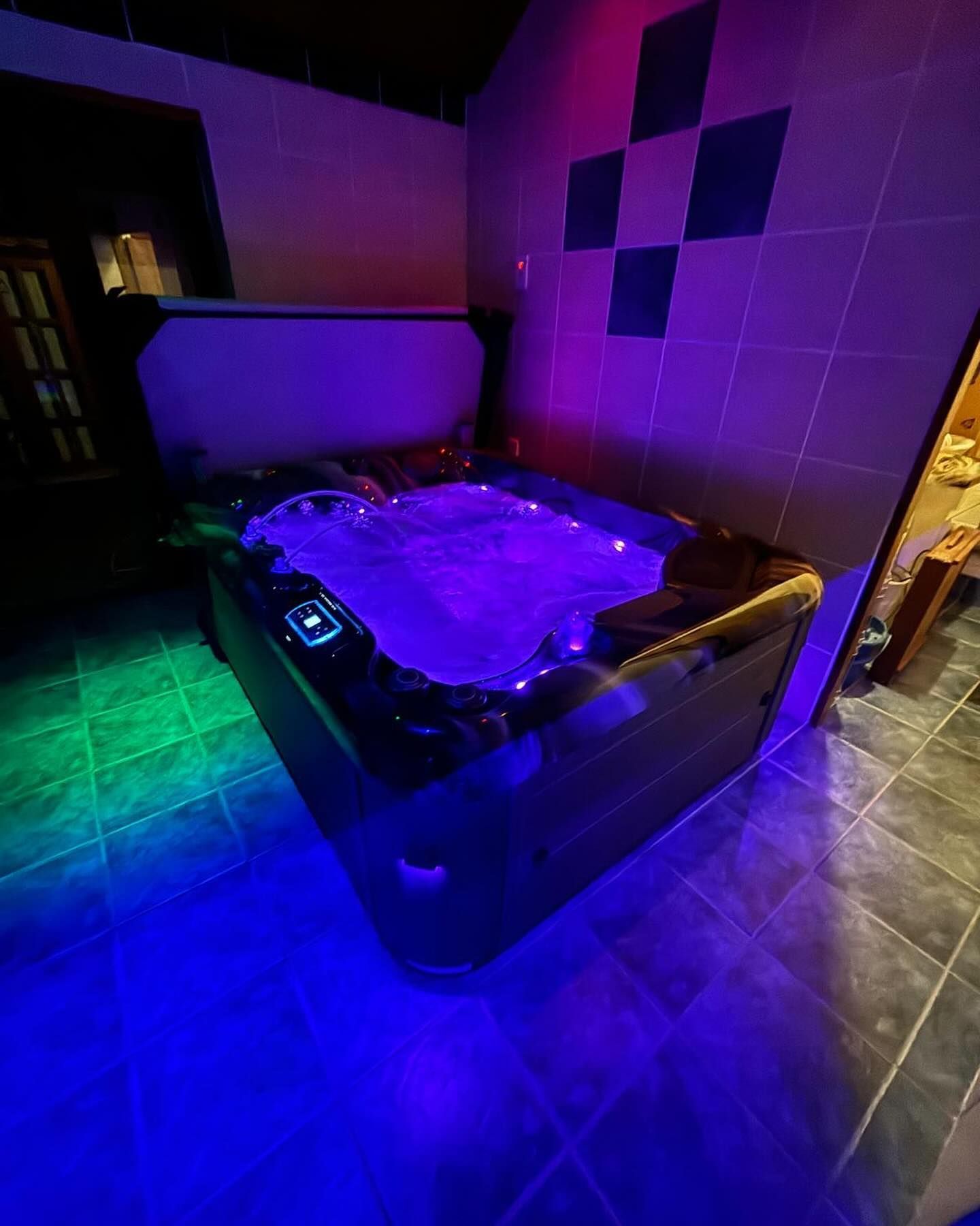 Hot tub with blue and purple lights in a tiled room.