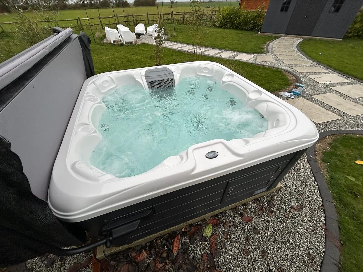 Hot tub with bubbling water, set outdoors on a gravel bed. Cover open to the side, path in background.