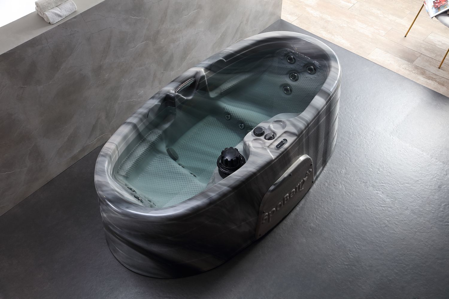 Oval hot tub with marbled gray exterior, filled with water, in a modern bathroom.