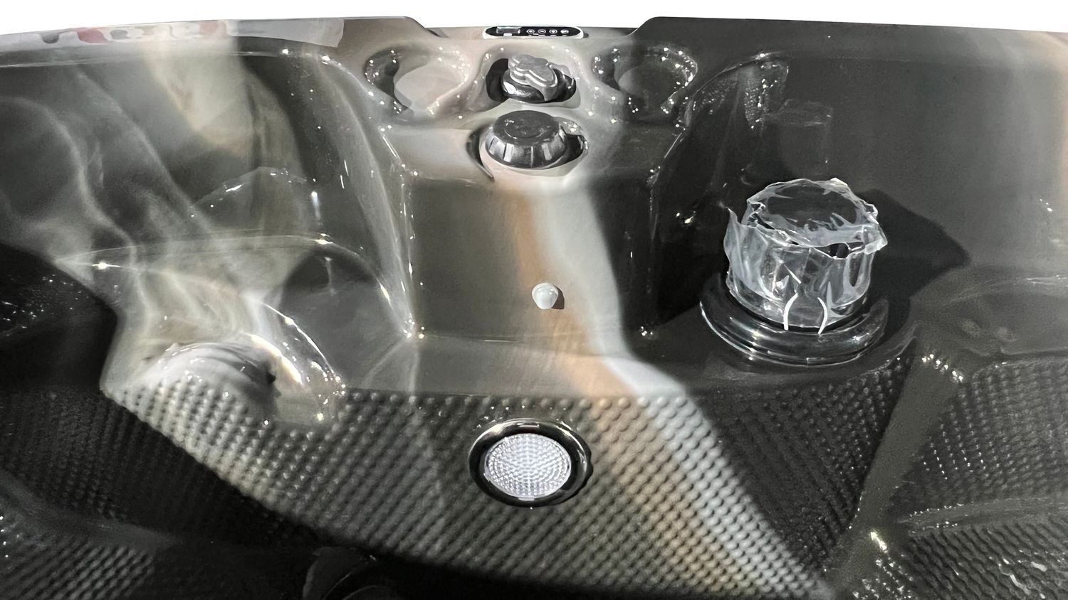 Close-up of a hot tub interior with gray and black textured surfaces and control knobs.