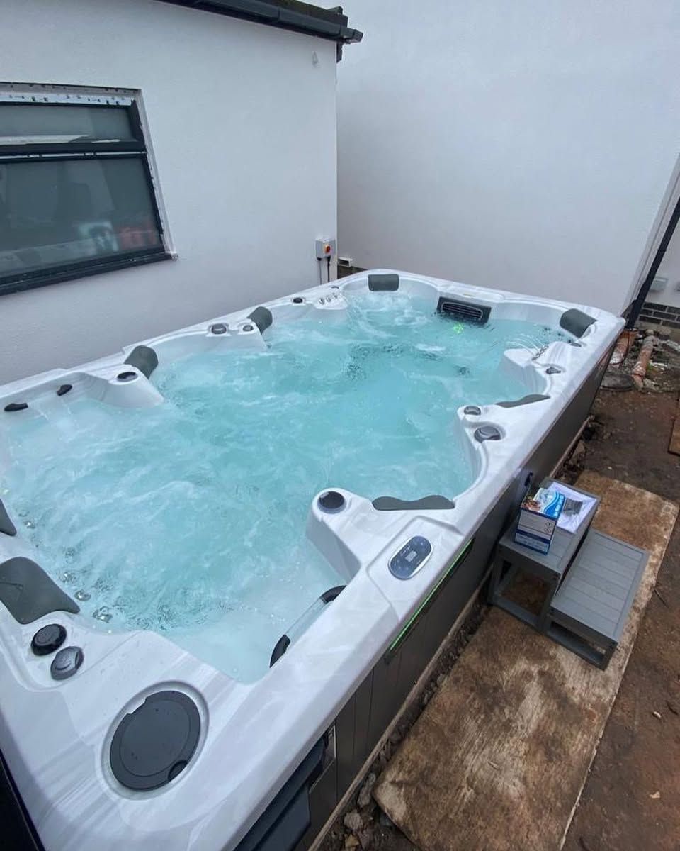 Large rectangular hot tub with bubbling water sits outside a white building. A small set of gray steps is next to it.
