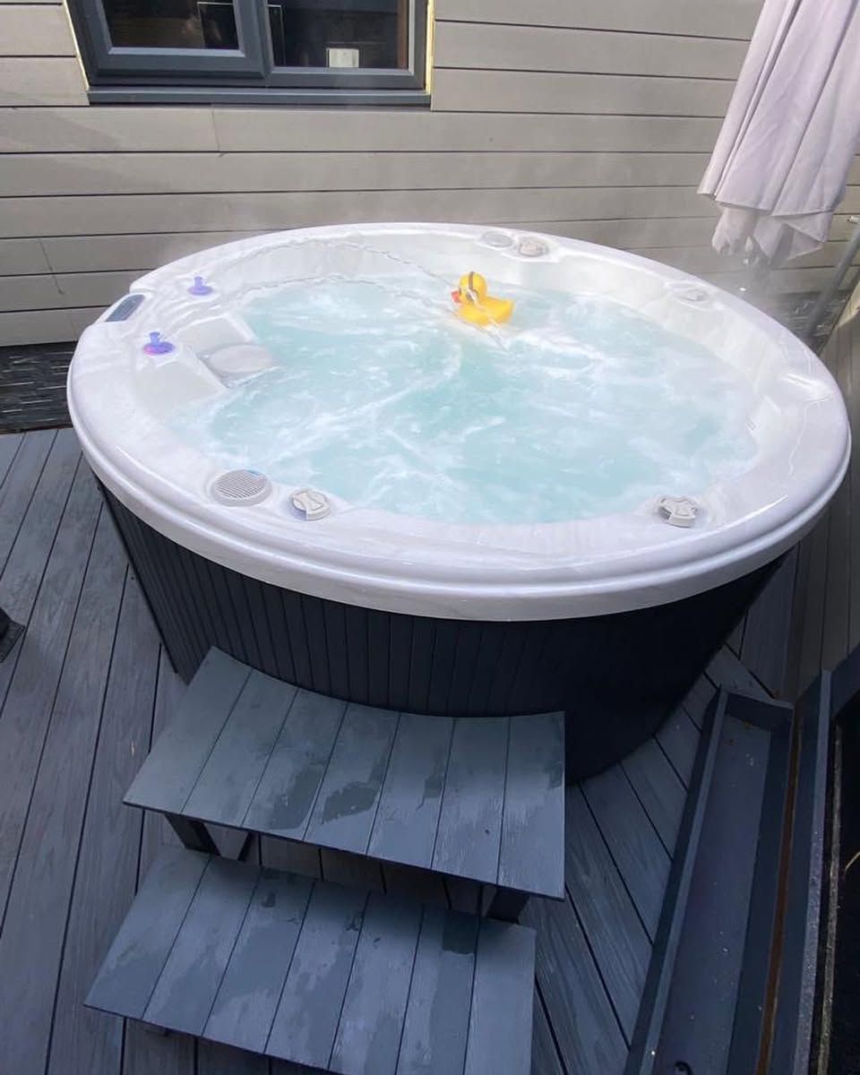 Hot tub with steam, a yellow rubber duck, and wooden steps on a deck.