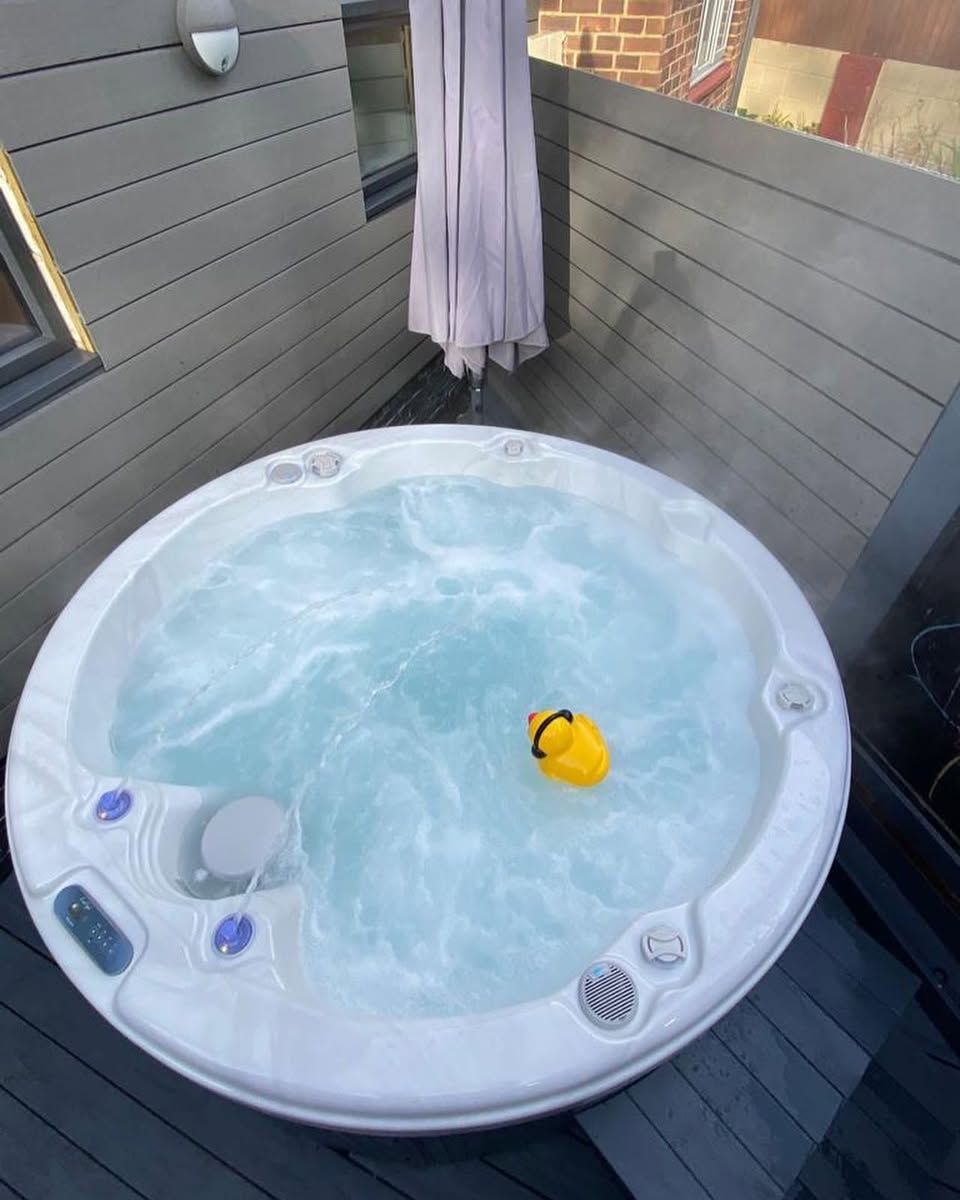 A round, white hot tub filled with water. A yellow rubber duck floats inside.