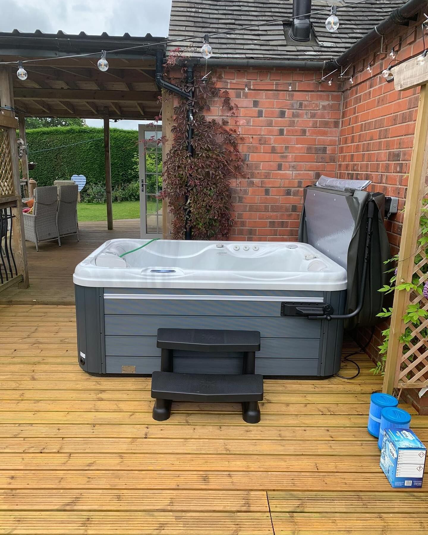 Hot tub on wooden deck, next to a brick wall. Steps lead up to it.