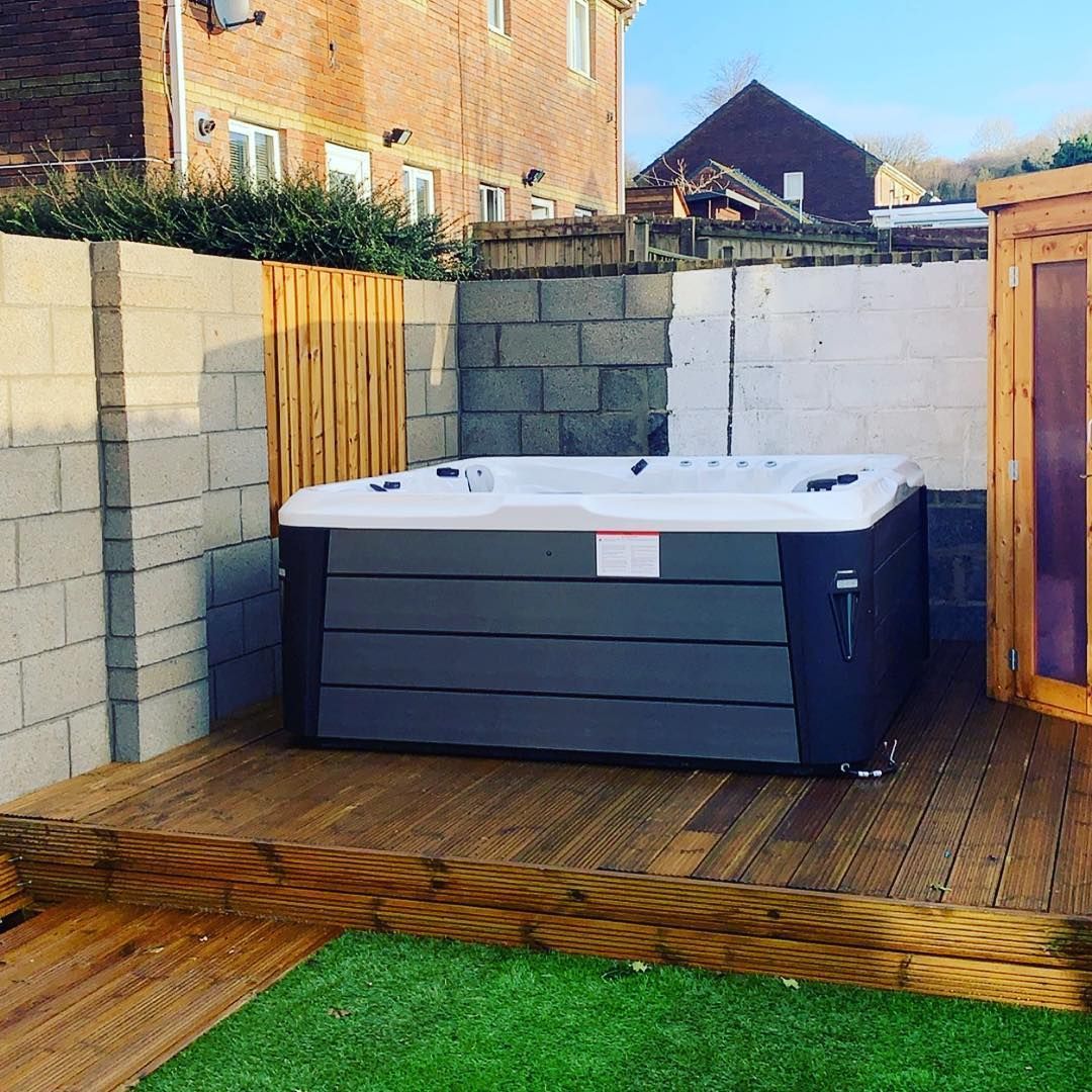 Hot tub on a wooden deck next to a brick wall. Green lawn in front.