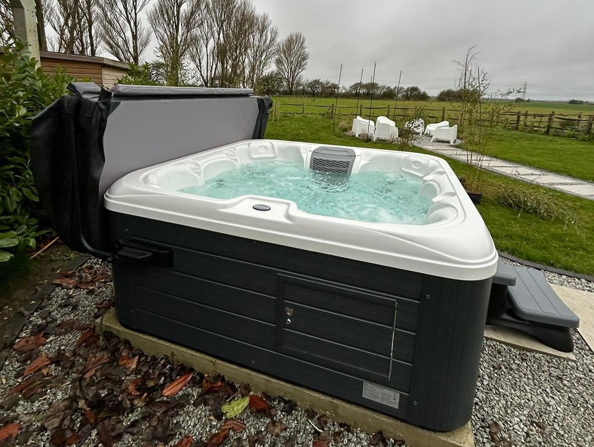 Hot tub with open cover, bubbling water, outdoors on concrete base, gray and white.