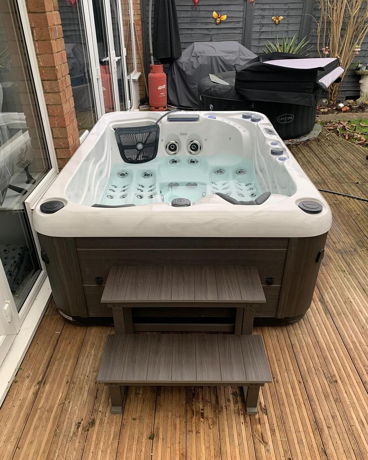 Hot tub on wooden deck, dark brown and white, with steps. Outdoor setting.