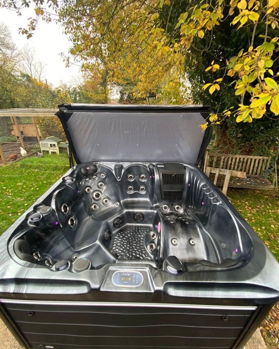 Black hot tub with jets and open lid, set outdoors in a yard with fall foliage.
