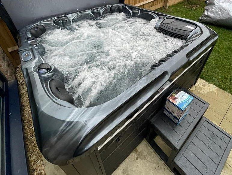 Hot tub with bubbling water, dark gray exterior, next to a small set of steps, outdoors.