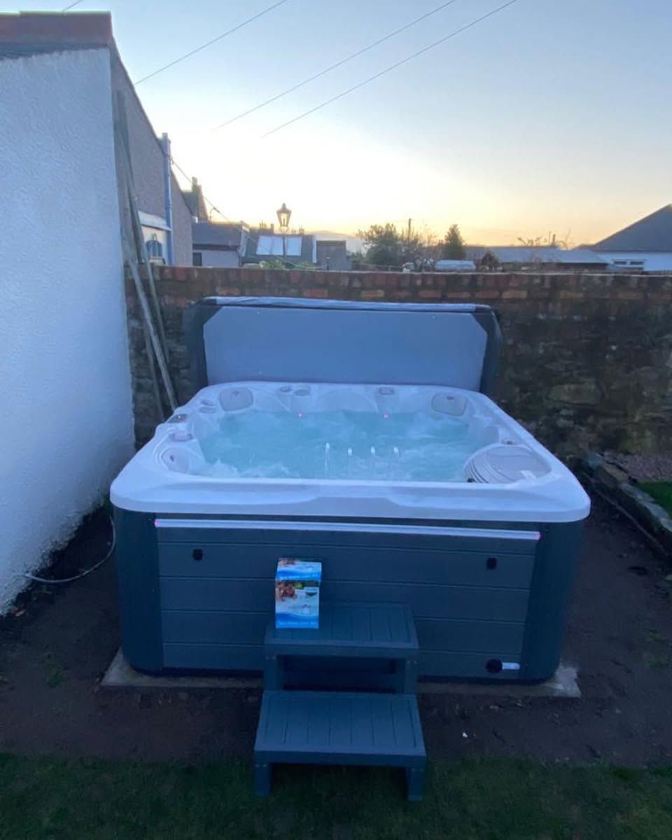 Hot tub outdoors, gray cover open, with steps. Evening sky in background.