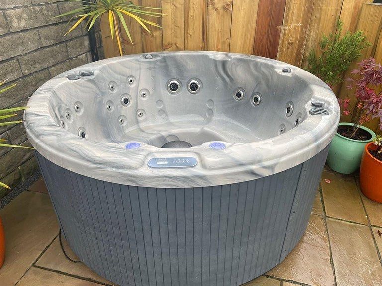 Round hot tub with blue-gray exterior and marbled gray interior, on a brick patio.