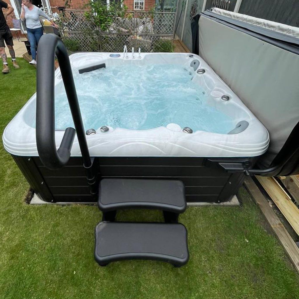 Hot tub with steps and handrail on grass. People in the background.