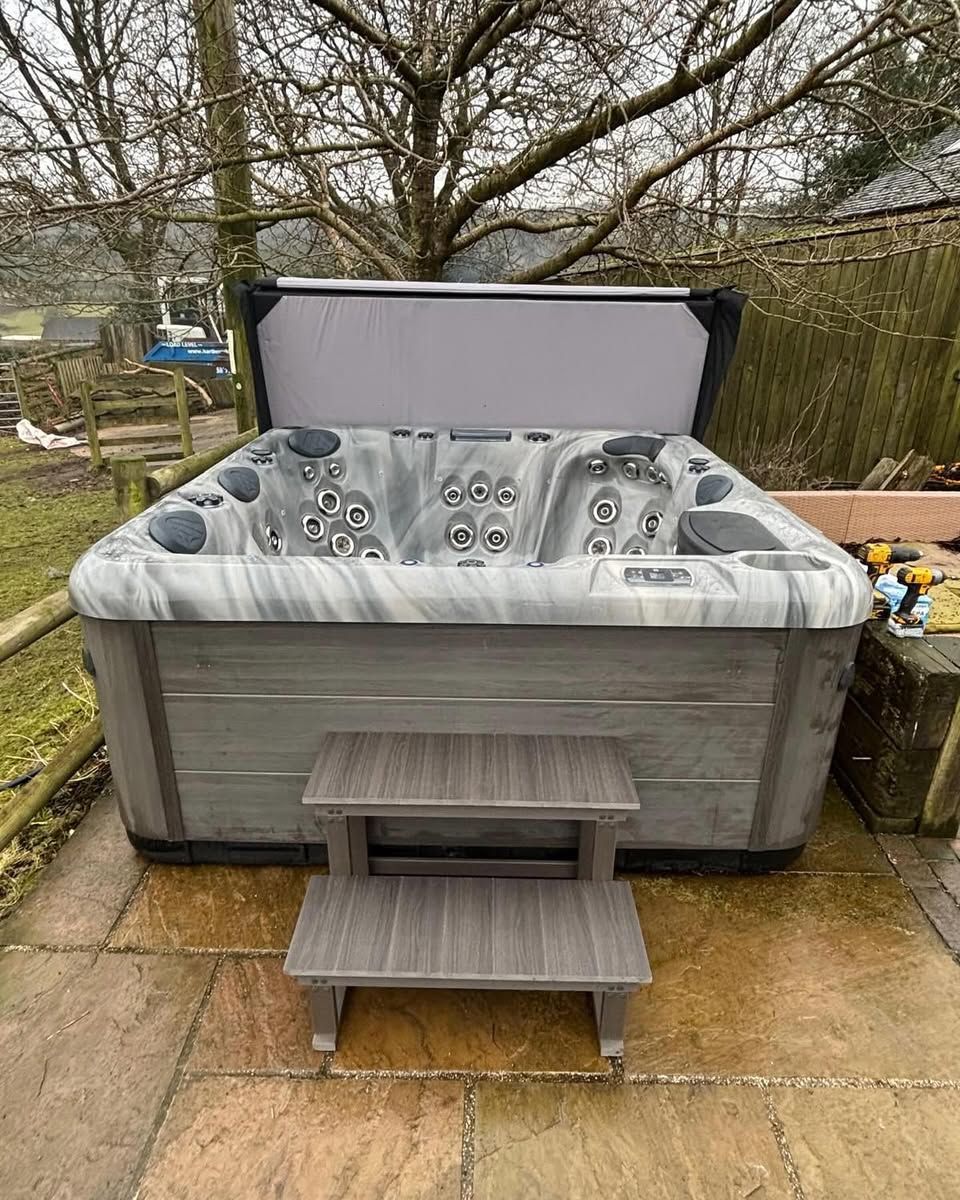Gray hot tub with open cover and matching steps on a stone patio.