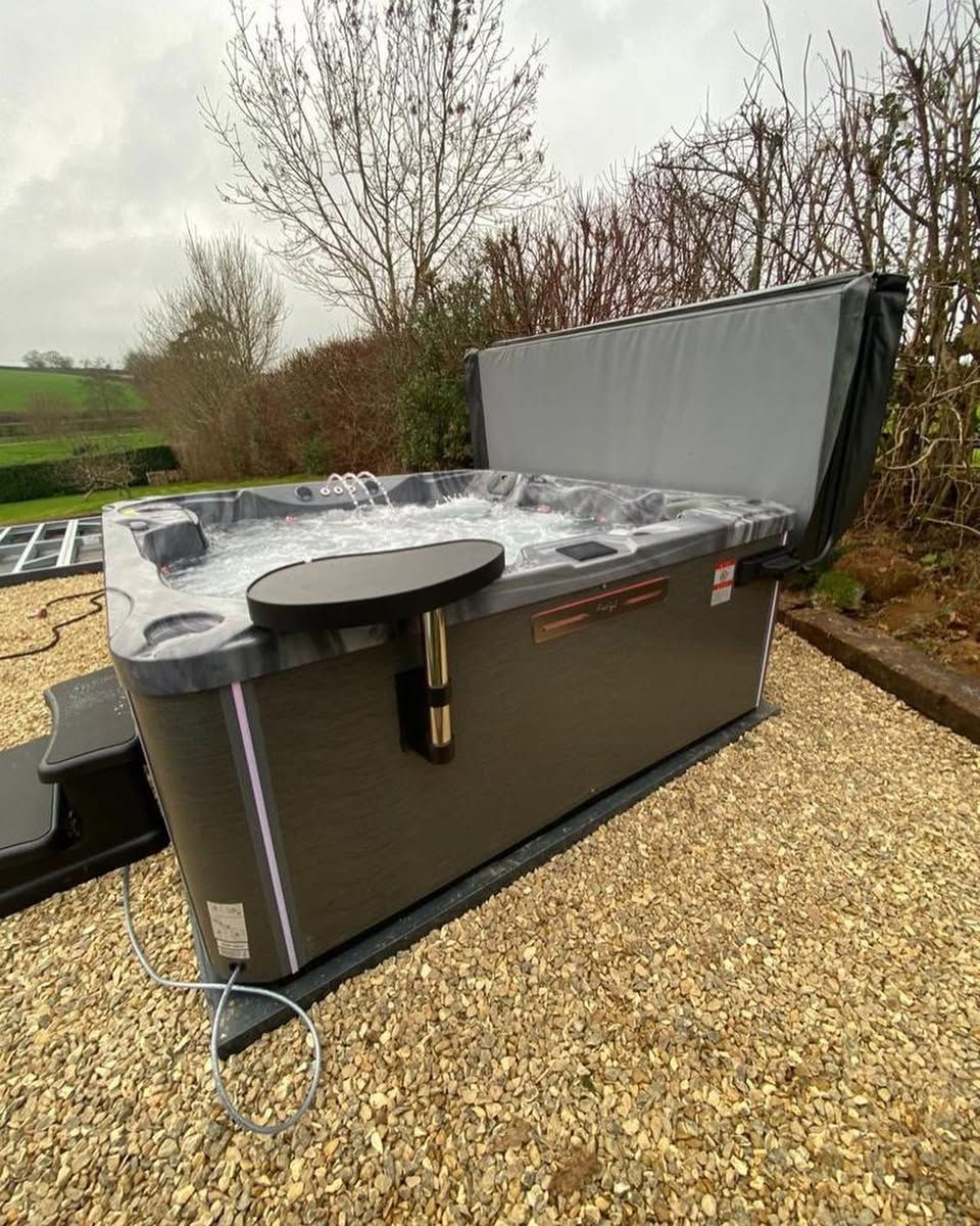 Hot tub with cover open, next to a small table. Exterior setting with gravel. Gray and black.