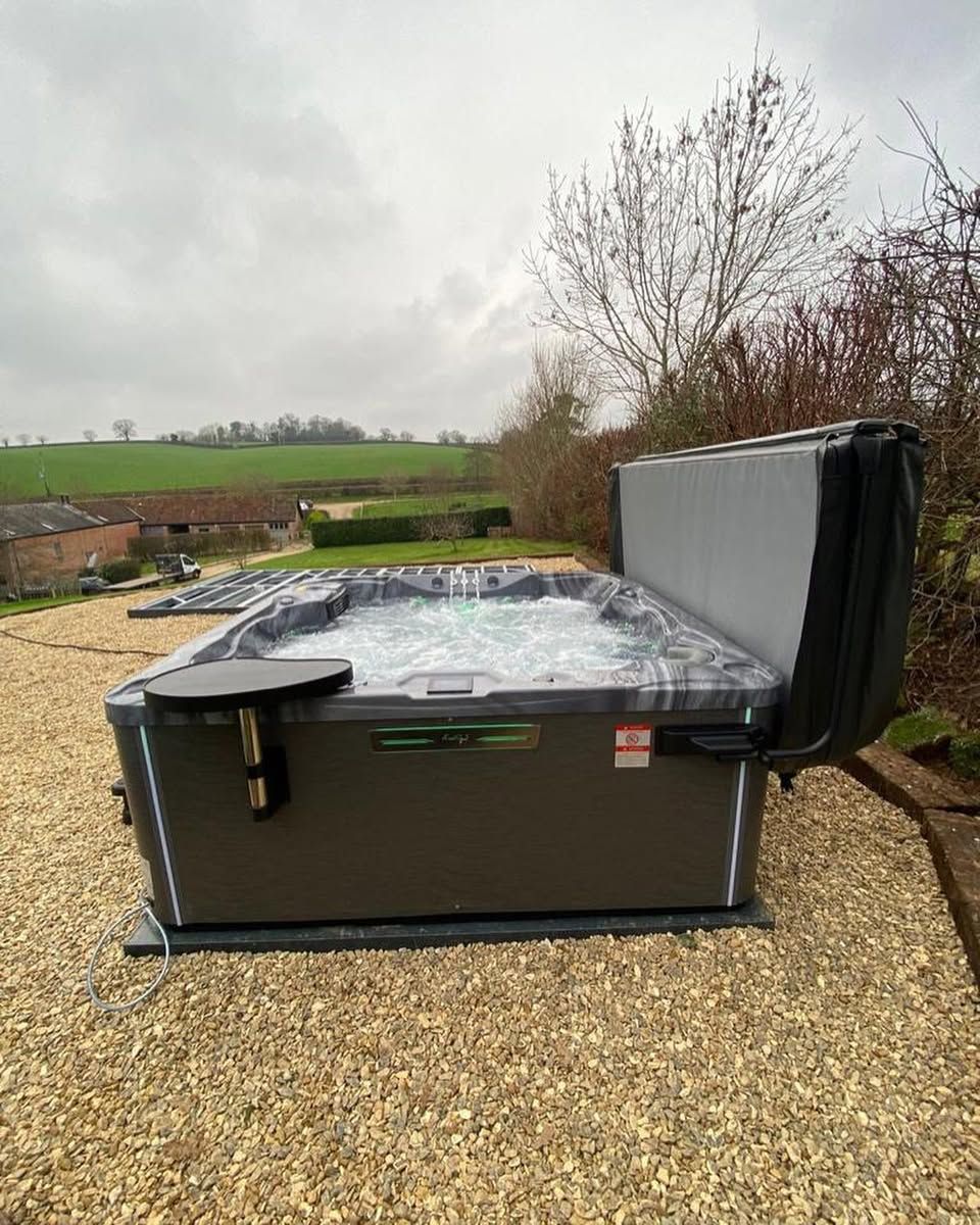 Dark gray hot tub on gravel with cover open.  Outdoor setting, cloudy sky.
