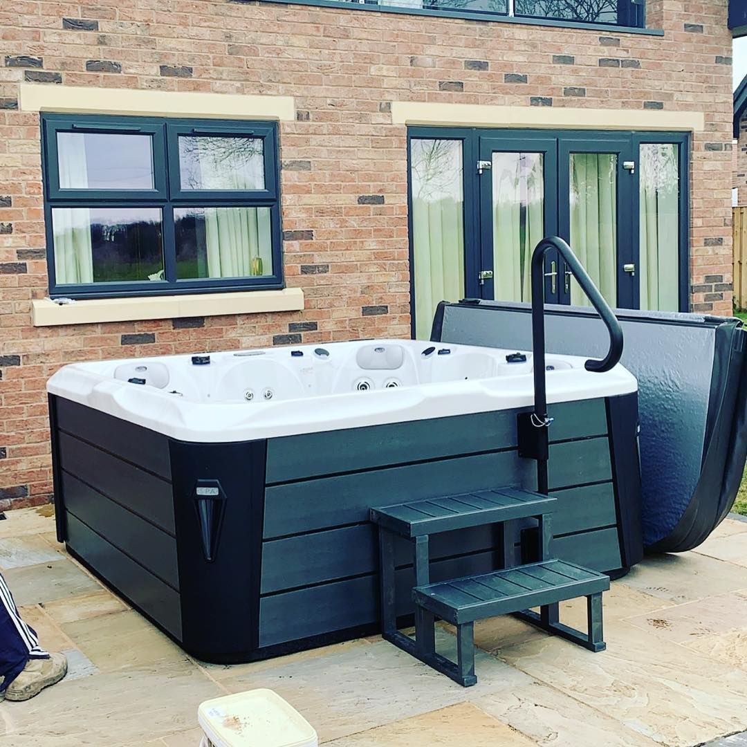 Dark gray hot tub with steps next to a brick building.