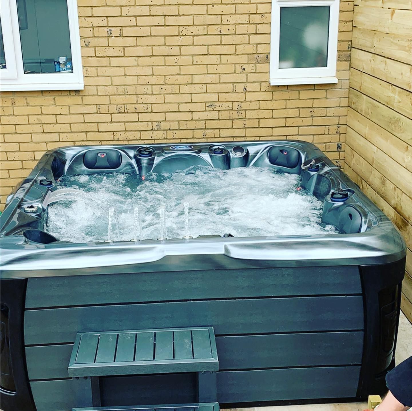 Hot tub with bubbling water, set in a brick and wooden panel-walled outdoor area, steps visible.