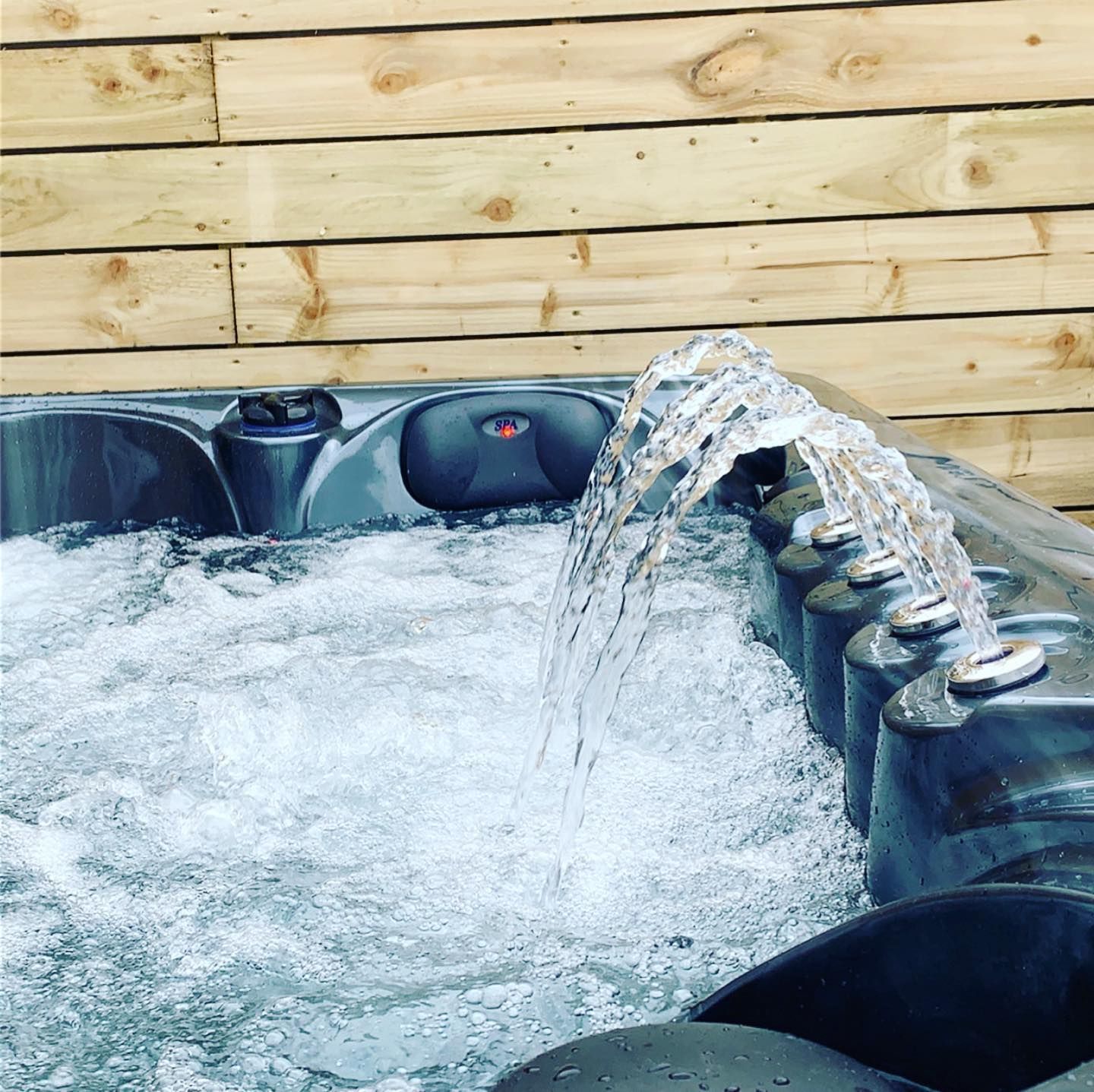 Hot tub with water fountain feature. Wooden wall in background. Water bubbles and splashes.