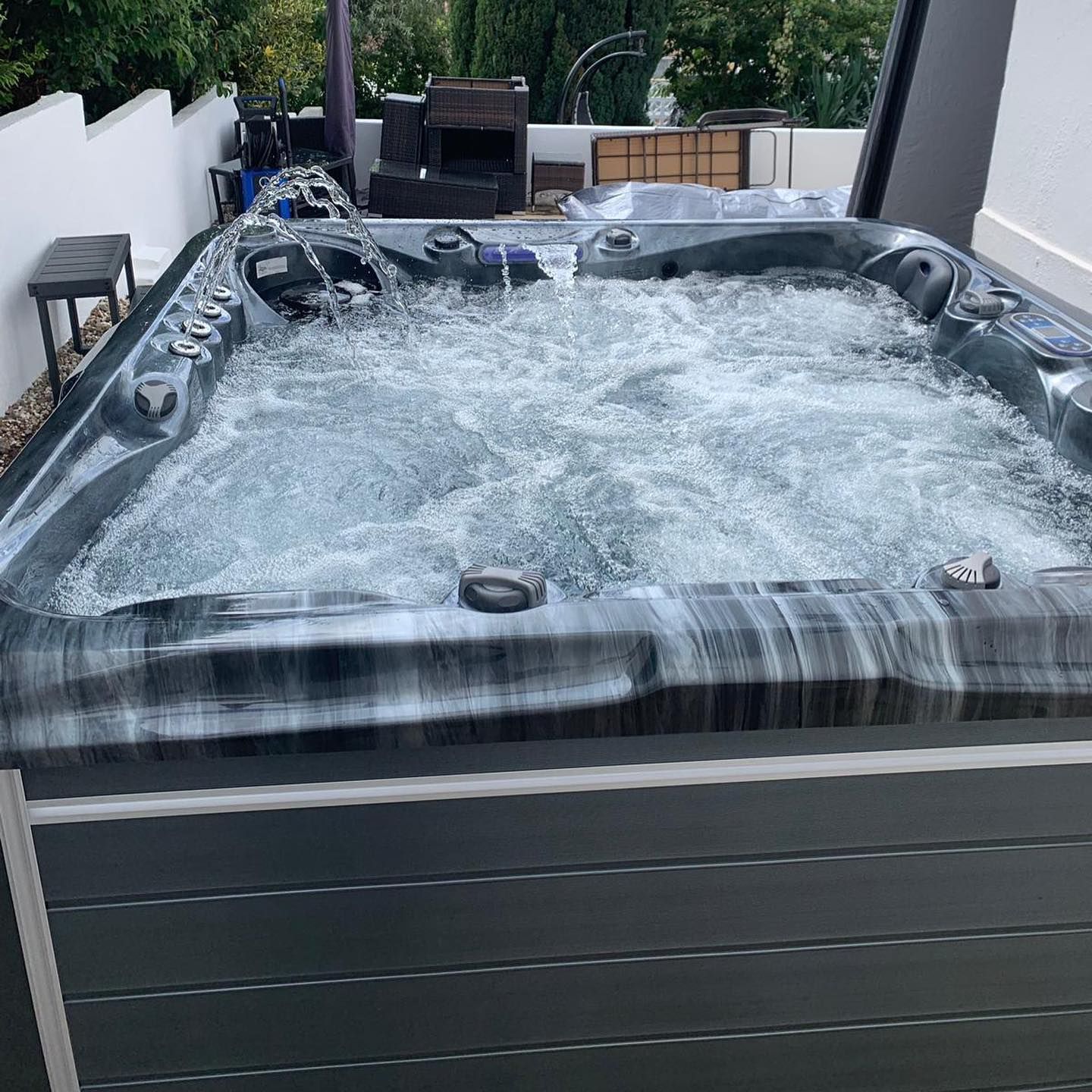 Bubbling hot tub with gray and black marbled trim in an outdoor setting.