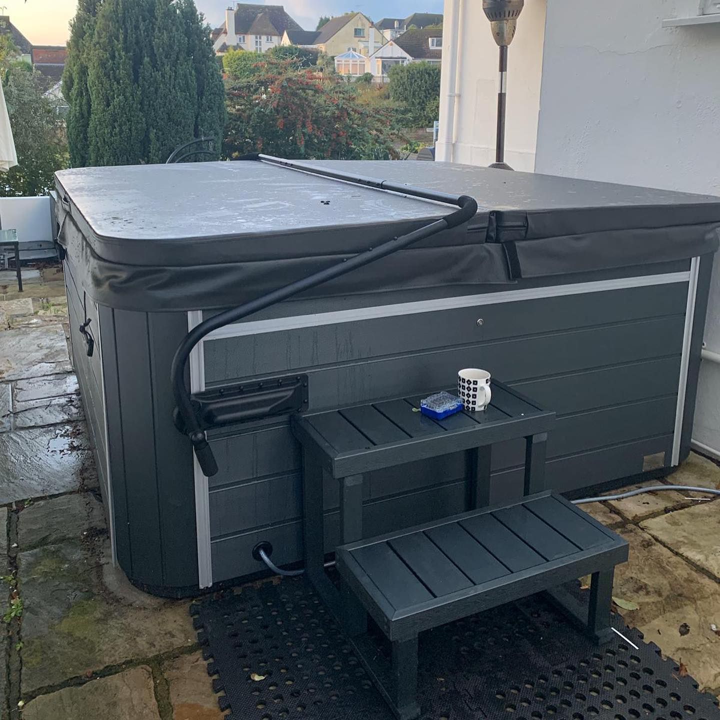 Hot tub with dark gray exterior, steps, and cover in an outdoor patio setting.