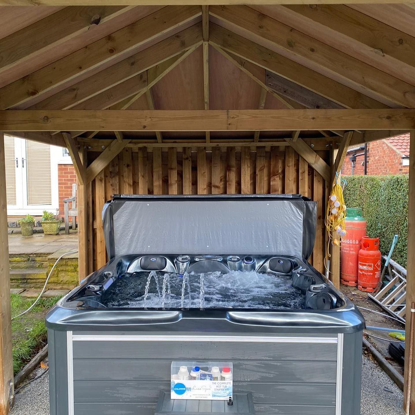 Hot tub with water jets under wooden gazebo, set in a backyard.