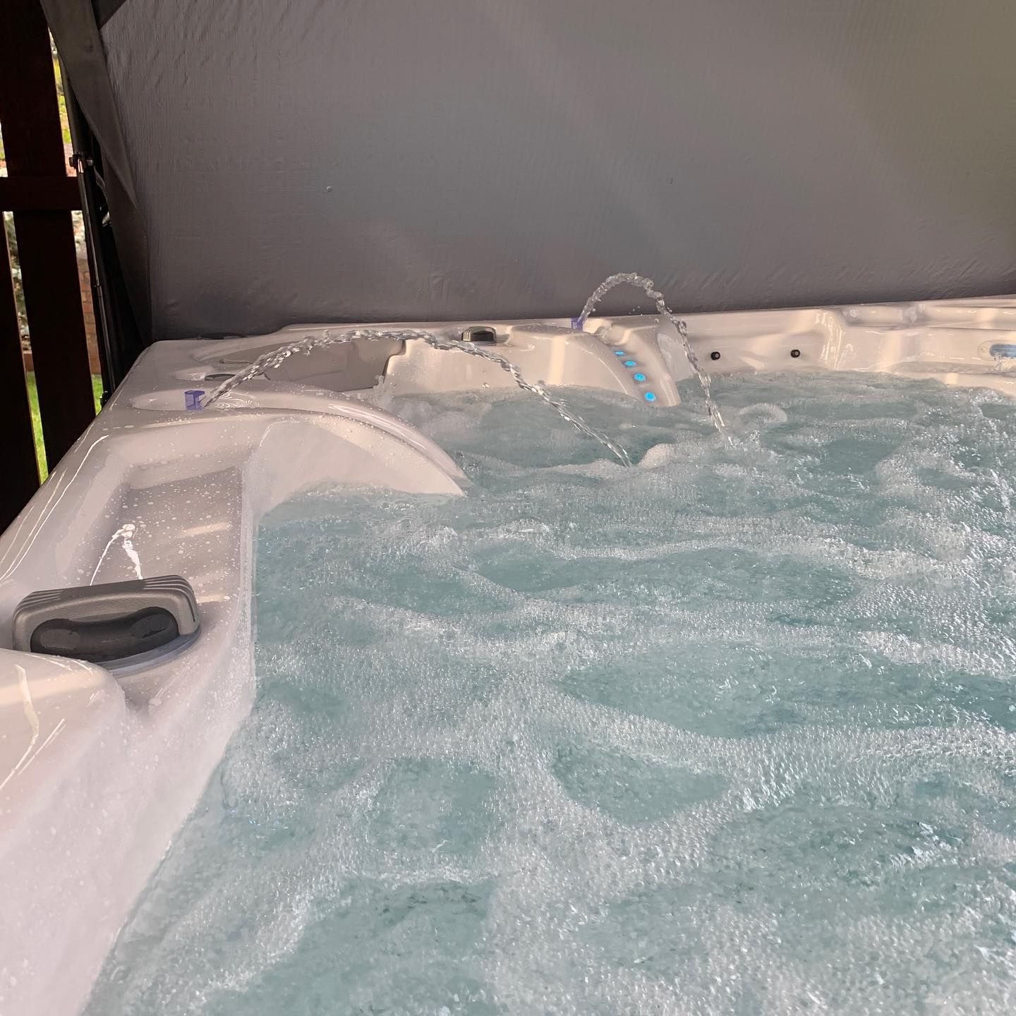 Bubbling hot tub with water jets, under a gray canopy.