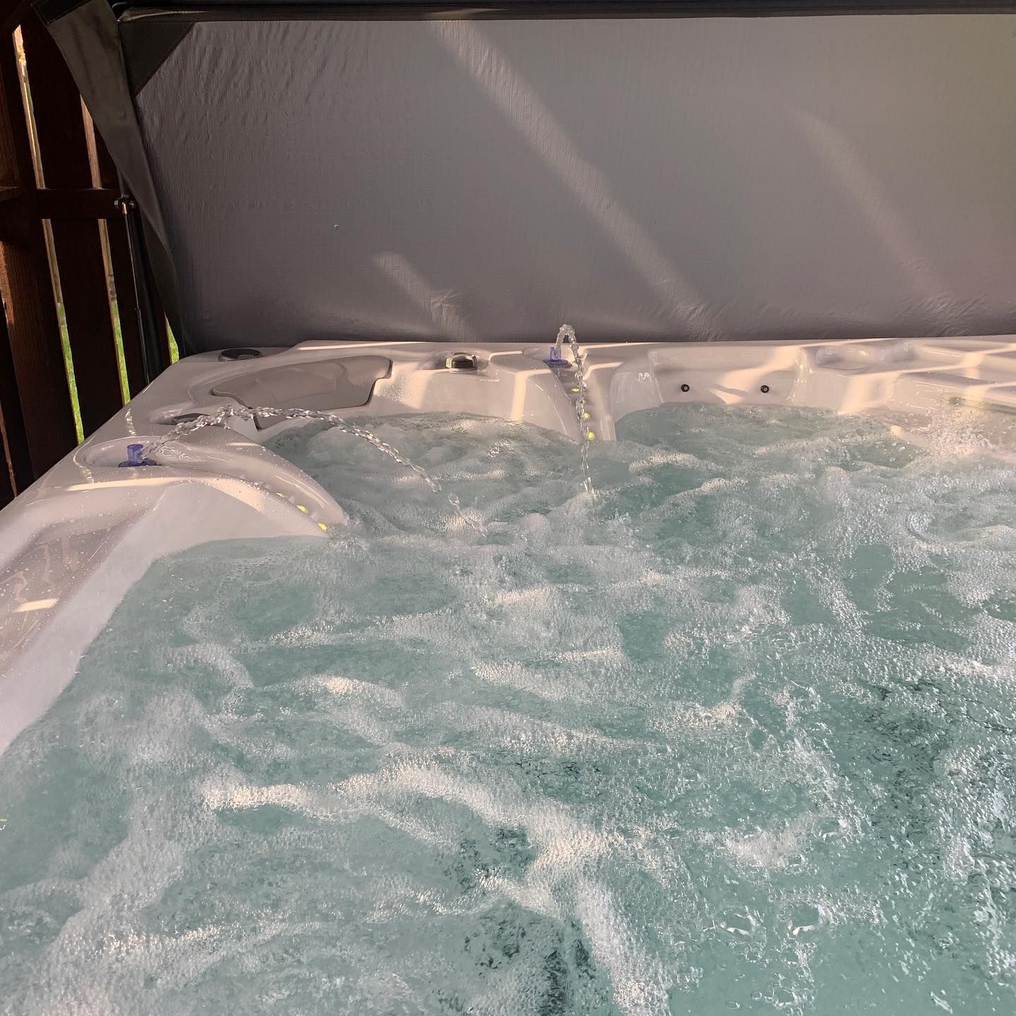 Bubbling hot tub with jets, water cascading from a spout, covered by a gray canopy.