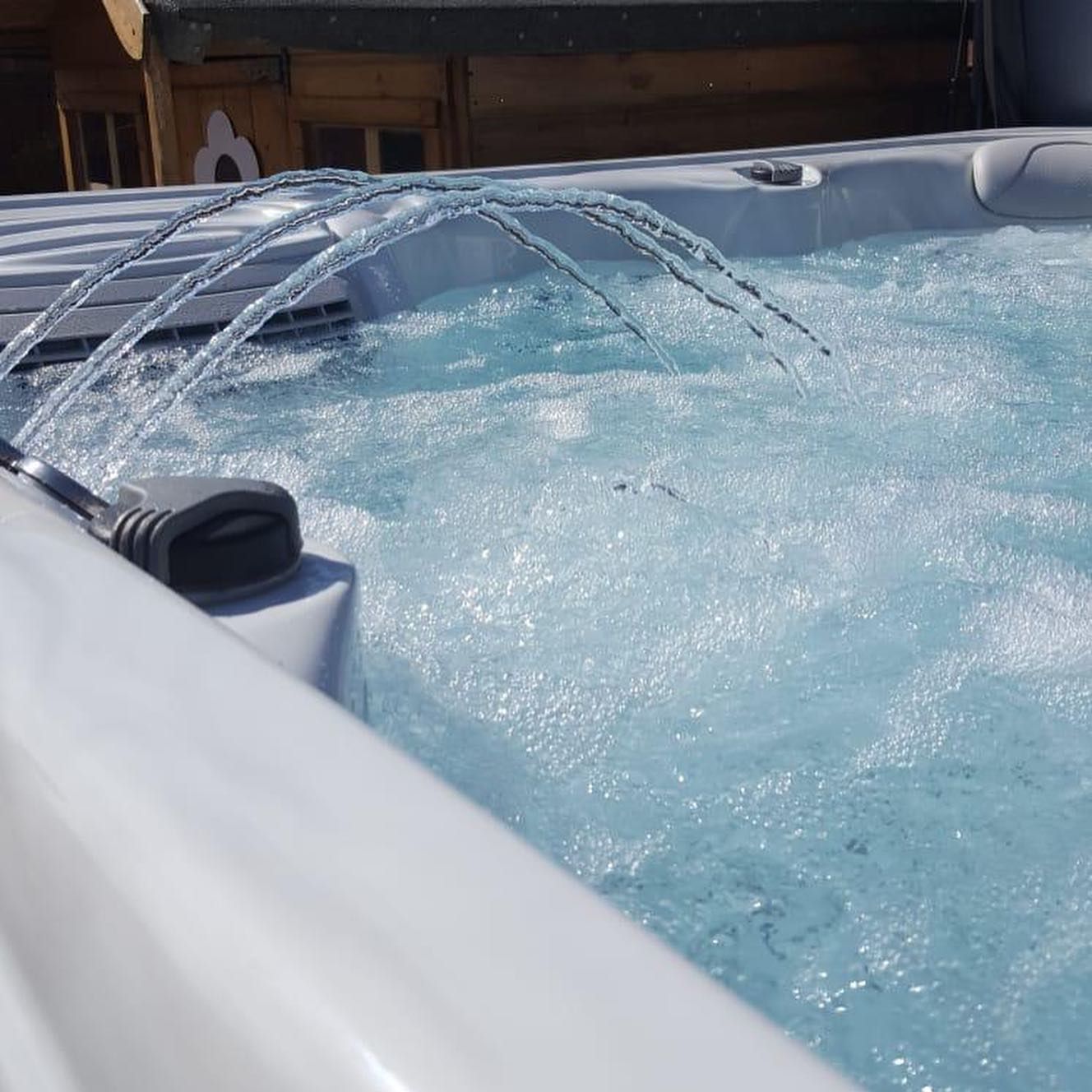 Bubbling hot tub with water fountain feature. White spa exterior, clear water, sunny setting.