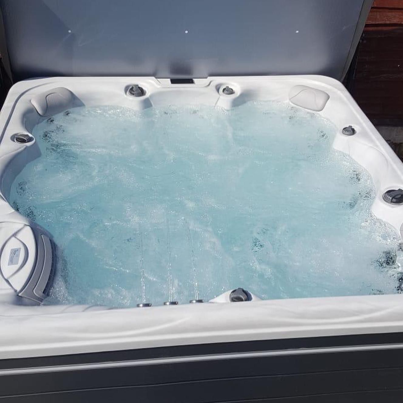 Bubbling hot tub with open lid, filled with blue water.