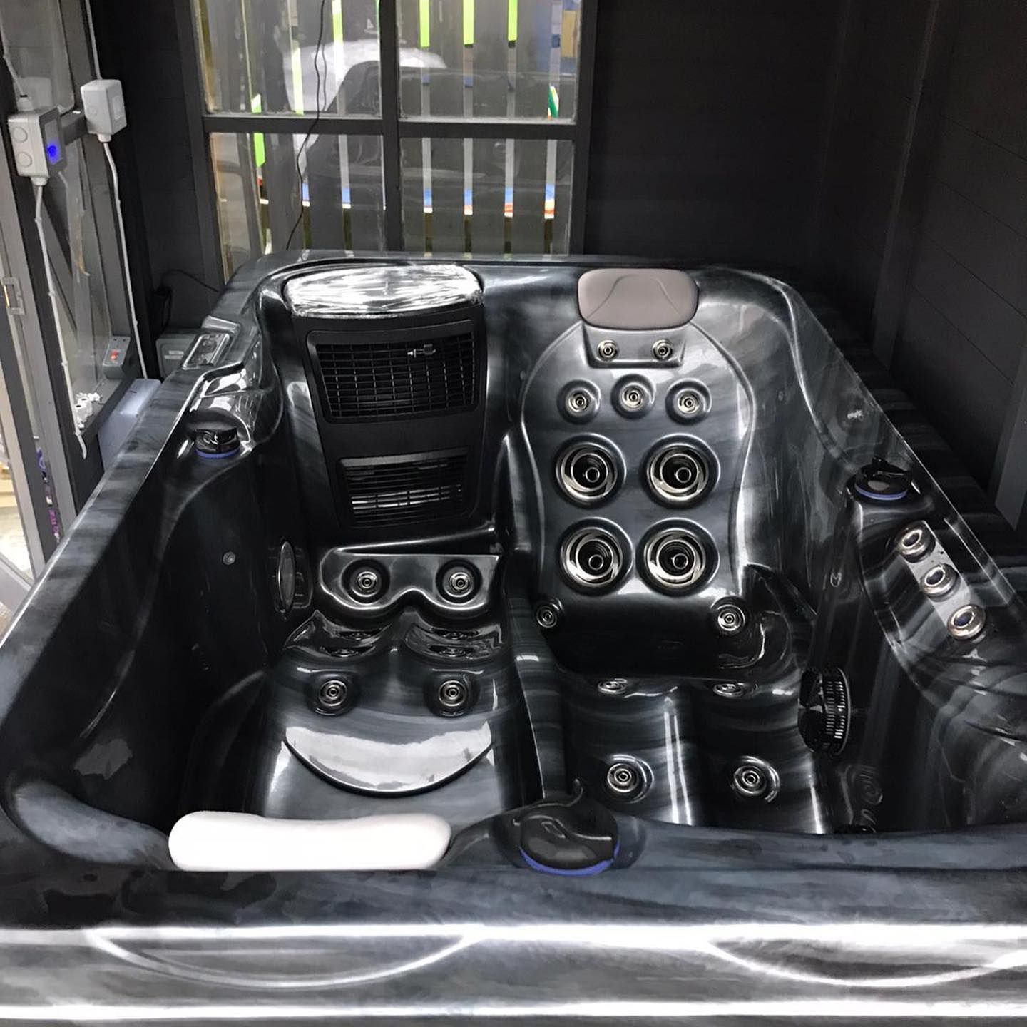Black hot tub with numerous jets, inside a dark enclosure.