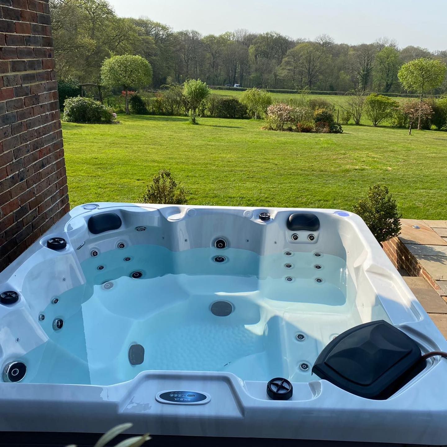 Hot tub filled with water on a patio overlooking a green lawn and trees.