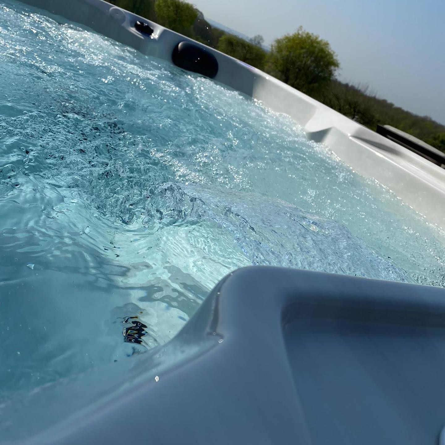 Bubbling clear water in a white hot tub, outdoors on a sunny day.