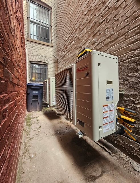 Narrow alley with utility equipment and trash bins between brick walls.