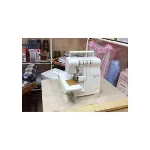 Macchina da cucire overlock bianca su un tavolo da lavoro in una sartoria, con tessuti e indumenti sullo sfondo.