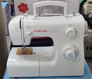 Macchina da cucire Singer bianca con logo rosso e quadranti argentati, appoggiata su un tavolo.