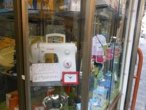 Macchina da cucire d'epoca in una teca di vetro con cartellino del prezzo e piccolo orologio rosso.