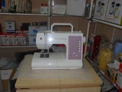 Una macchina da cucire bianca su un tavolo di legno in una corsia di un negozio, con scaffali di prodotti alle sue spalle.