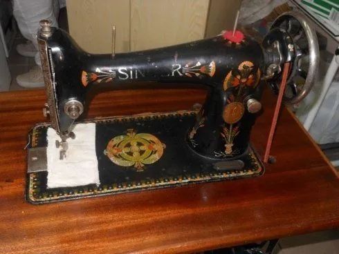 Macchina da cucire Singer vintage nera su un tavolo di legno, con dettagli dorati e base decorata.