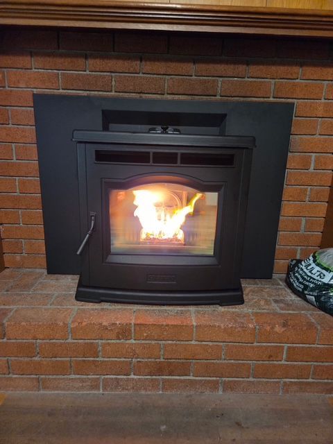 Lit fireplace insert with flames burning inside a brick hearth wall.